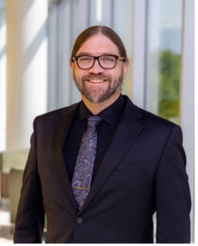 photo of male with glasses in a suit smiling for a headshot