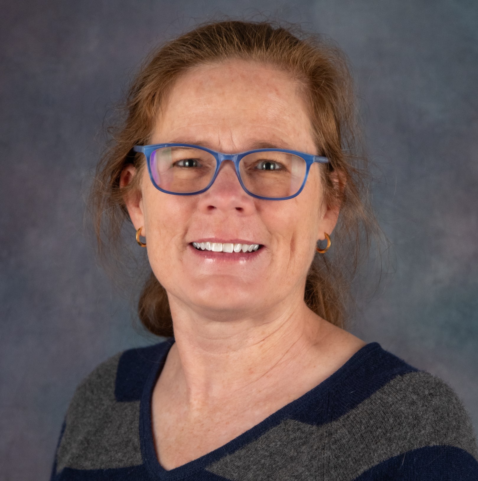Photo of Jill Slansky in blue glasses with red hai, pulled back into a low pont tail