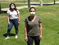 two students standing on grass, masked
