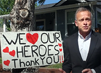 newscaster standing next to heros/heart handmade sign