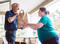 woman handing bag of groceries to senior man