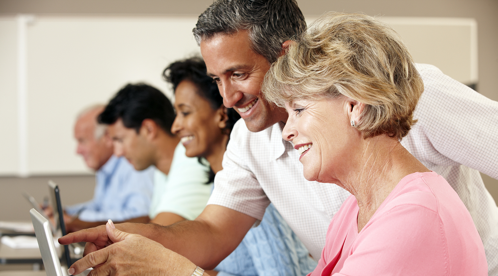 Group of seniors at computer with man helping them