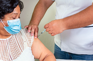masked woman getting vaccine in left arm
