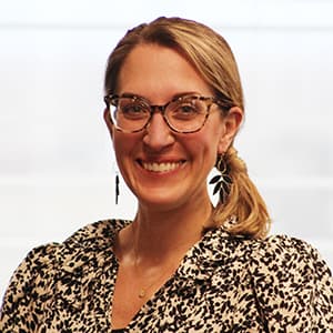 Woman with glasses and blonde hair pulled back smiling with her teeth.