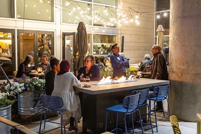 DC5 SQSH Group of people sit on the Coohills' outdoor patio at night with bistro lighting and a student playing guitar and singing.