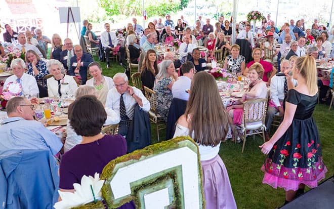 Large group of people seated at round tables at an outdoor event.