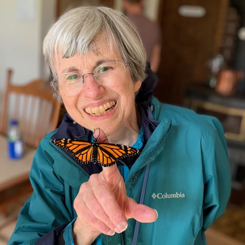 Paula Budzak smiling with her teeth as a Monarch butterfly resting on her hand.