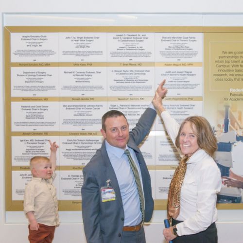 Mary Cope and Dr. Meguid point to their endowed chair plaque, with Meguid's toddler behind them, also pointing up.