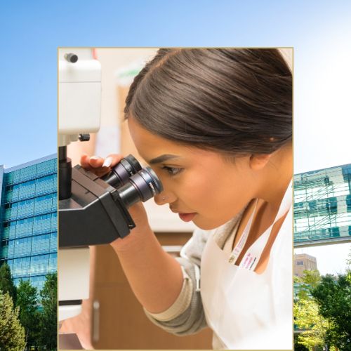 A female scientist wearing a 'Ludeman Center' lanyard peers into a microscope.