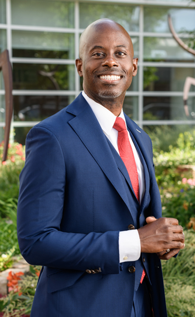 A photo of Reed wearing a blue suit and standing in front of green trees and bushes.