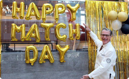 Dean Sampson in front of gold balloons spelling Happy Match Day