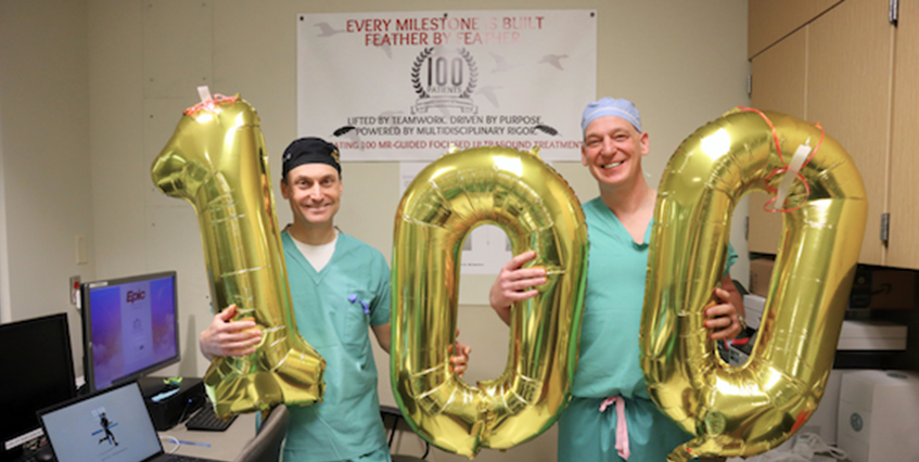 Two doctors holidng gold balloons spelling 100
