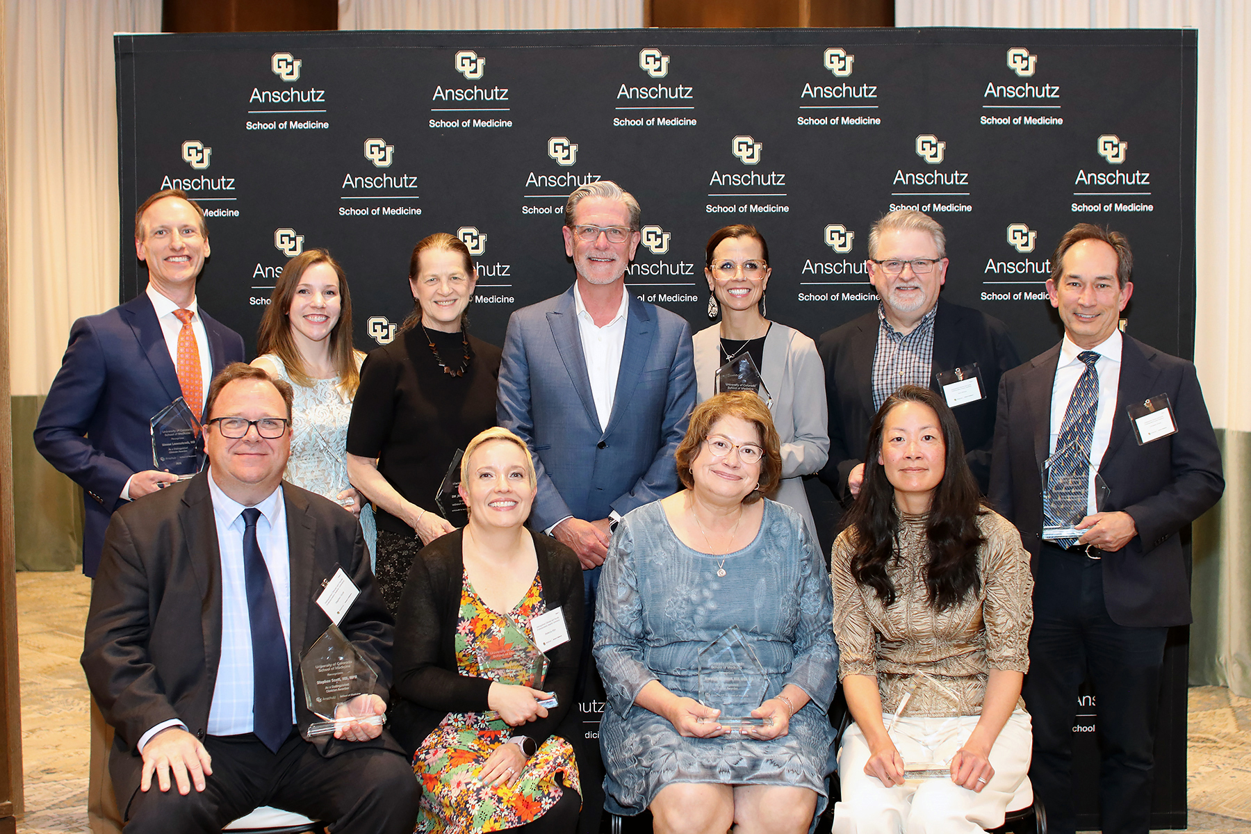 11 people smiling with awards in their hands