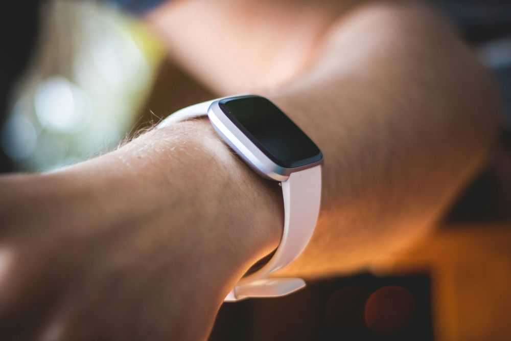A close-up of a wrist wearing a sleek, white smartwatch with a dark screen, set against a softly blurred background.