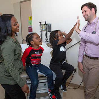 Medical resident high-fiving boy in exam room.