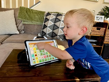 a boy tapping on the screen of an aac device with open communication software