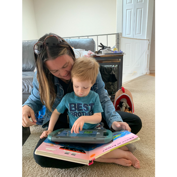 a child using an aac device on top of a large book while sitting in a womans lap