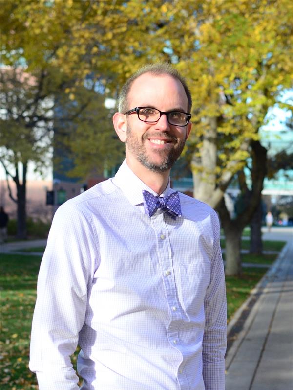 Man standing in white button up shirt with blue bowtie and glasses