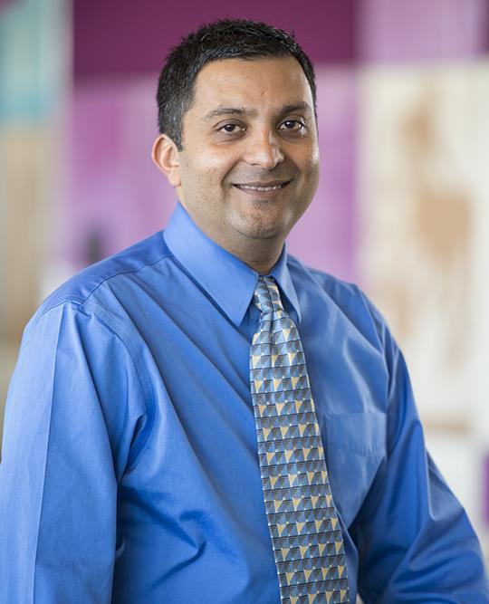 Middle aged man with brown skin and blue button up shirt and a patterned tie