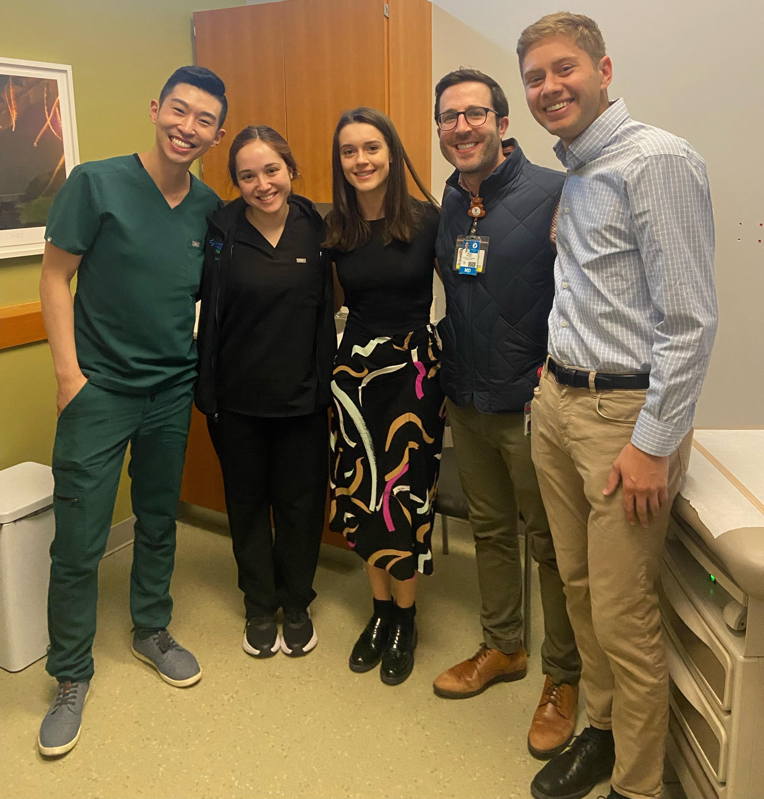 Two residents and two medical students standing in the DAWN Dermatology clinic, wearing scrubs and smiling