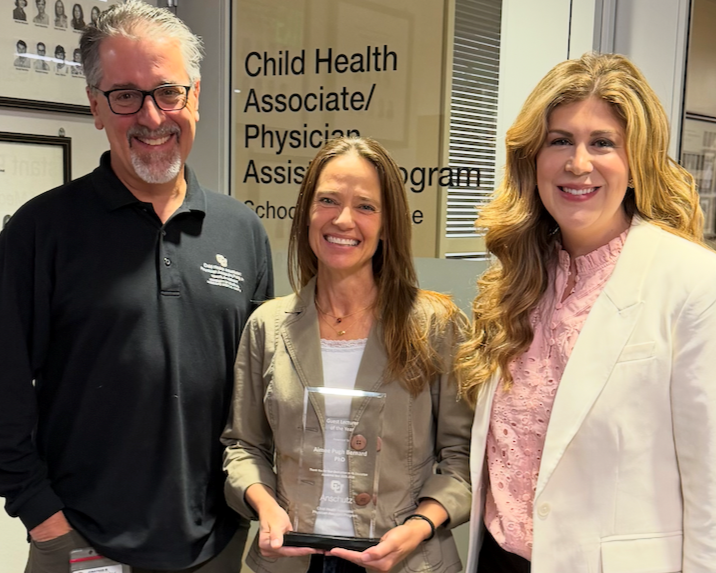 Photo of three people, with Aimee Bernard in the center holding an award