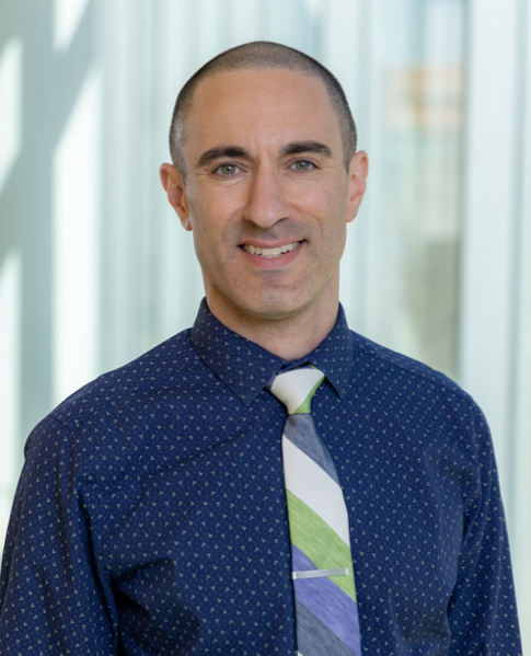 male doctor headshot with a polka dot button down on and green, cream, and blue striped tie
