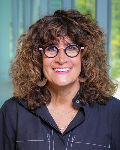 female with curly hair, a black button down shirt and black circle glasses, smiling for a headshot