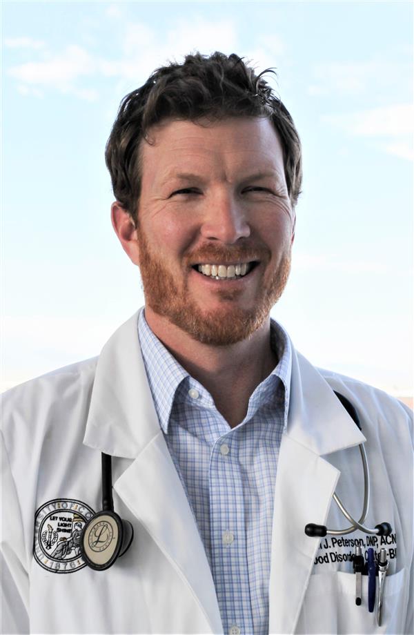 male in a doctoral white coat smiling for his headshot while outside on a sunny day