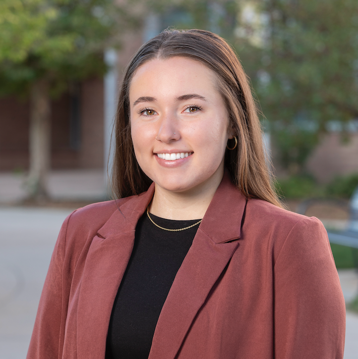 female wearing a salmon colored blazer and black shirt smiling and posing for a headshot