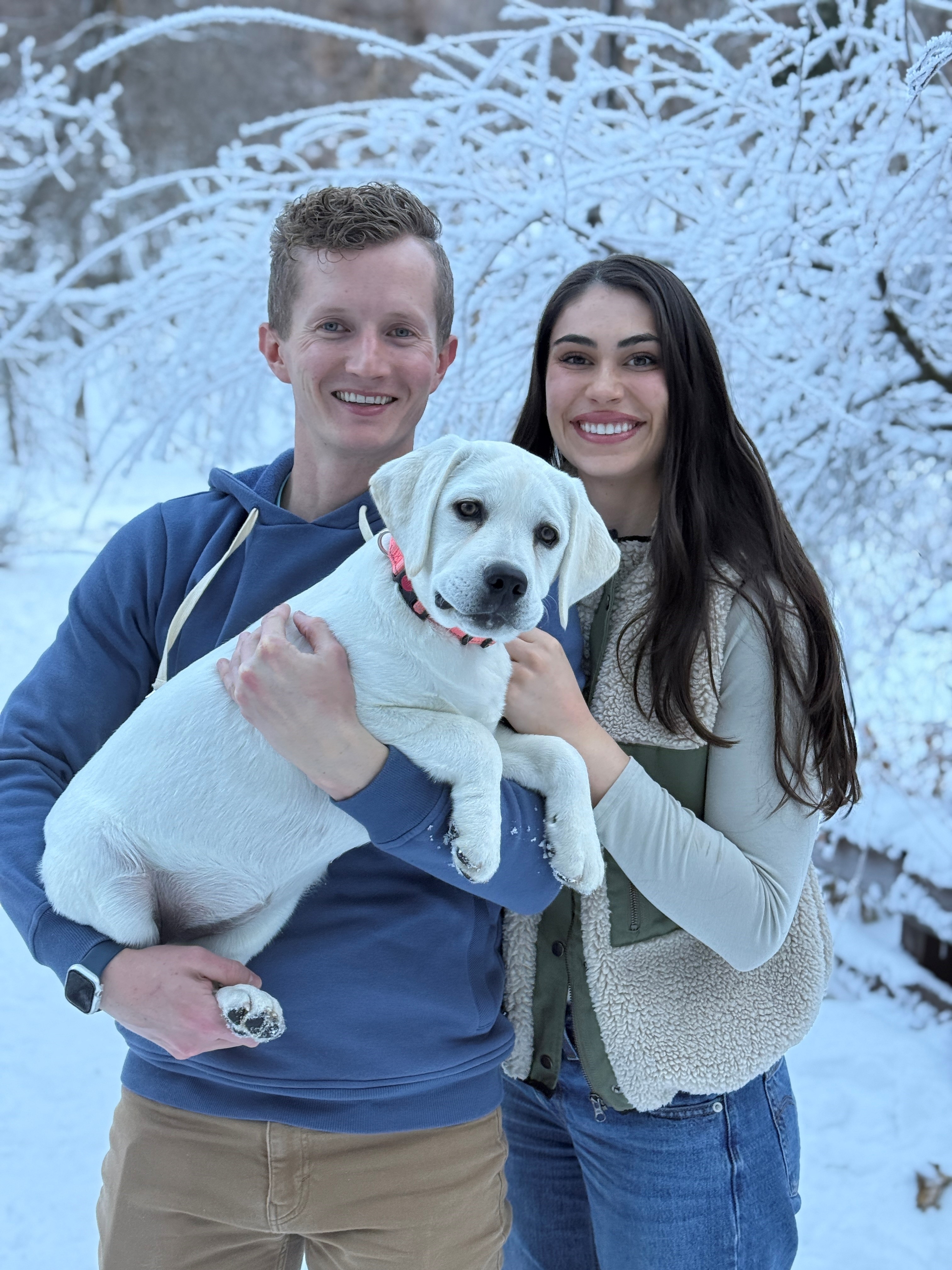 Dr. Anderson holding a dog in the snow next to a woman.