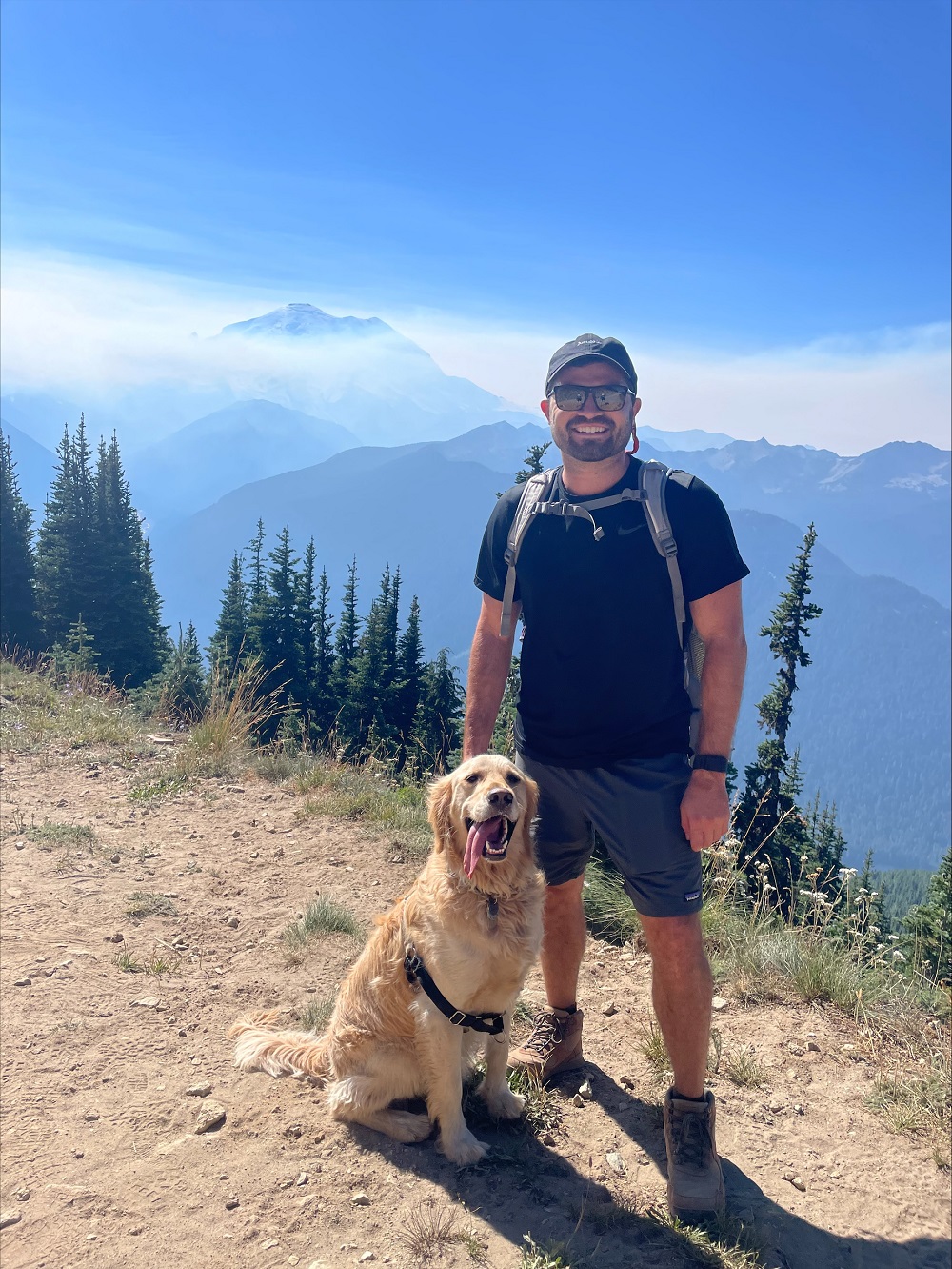 Photo of Dr. Boyer standing next to a Golden Retriever in the mountains.