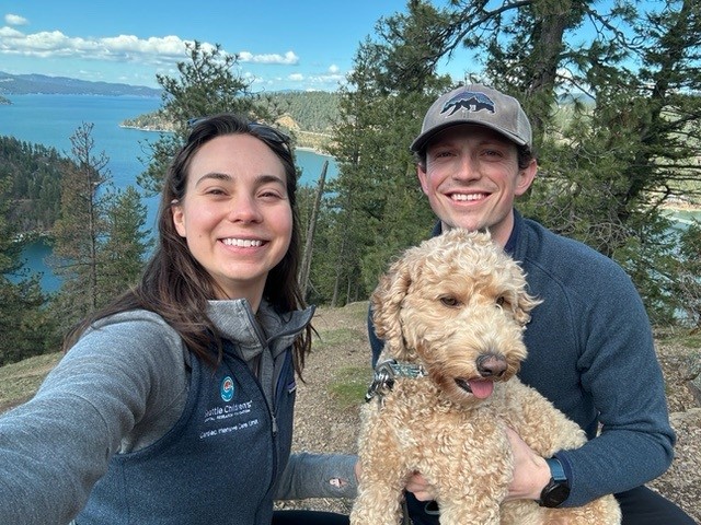 Photo of Dr. Kepple with a woman and a golden doodle by an alpine lake.