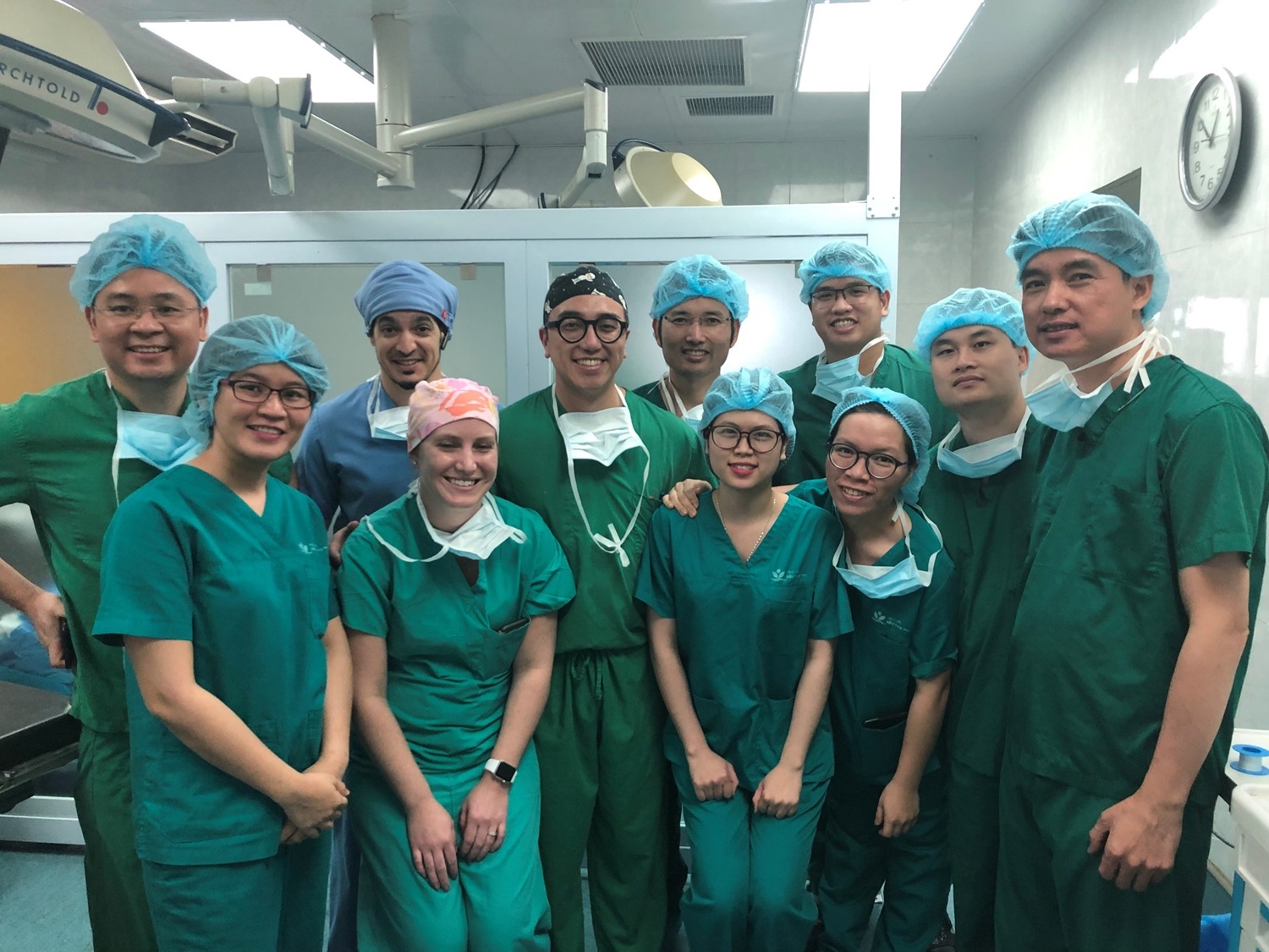 Group photo of doctors and trainees smiling in scrubs inside OR