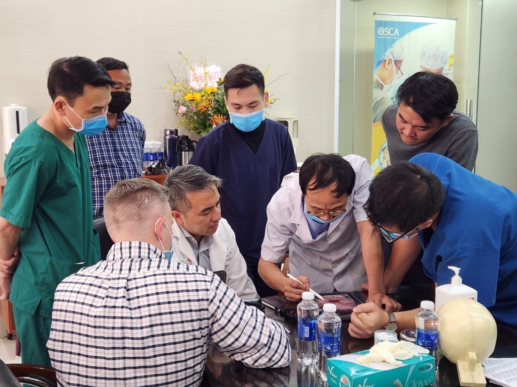 Group of people with masks and two doctors around a table looking at patient photo