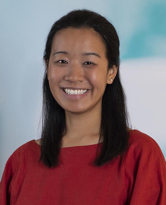 Professional headshot of a smiling woman with dark hair wearing a red top, photographed against a softly blurred background.