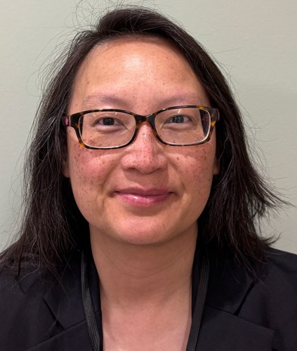 Headshot of a woman wearing glasses and a dark blazer, looking at the camera against a plain light-colored background.