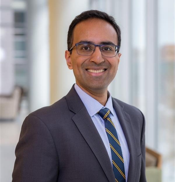 Professional Headshot of man in tie. Background is a blurred hallway.