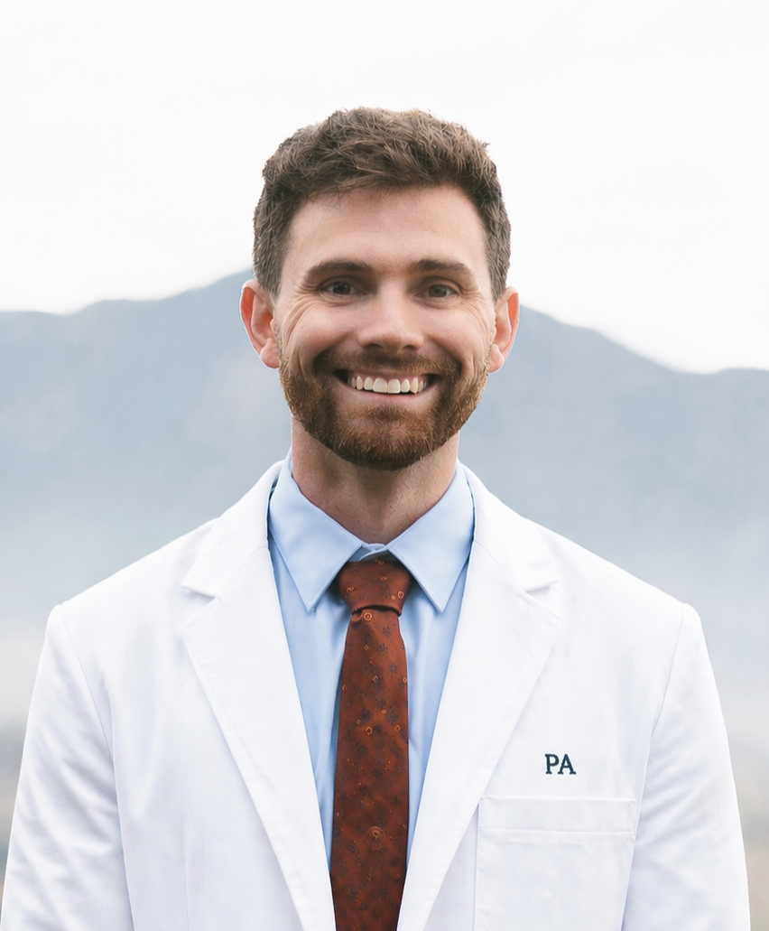 Portrait of a physician assistant wearing a white coat and tie, smiling outdoors with mountains softly blurred in the background.