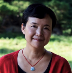Portrait of a person wearing a red cardigan and pendant necklace, smiling softly outdoors with a green, blurred natural background.