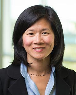 Professional headshot of woman in blazer. Background is blurred, floor to ceiling window.
