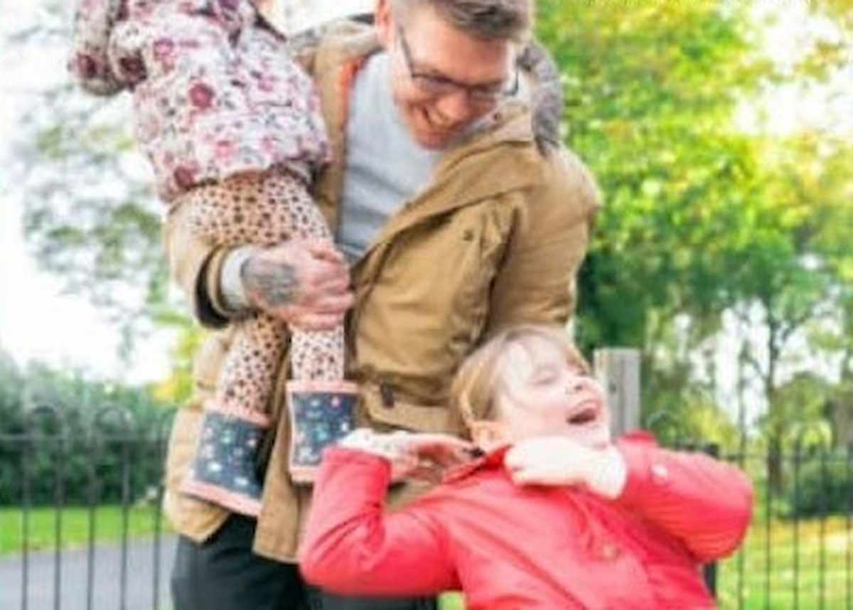 Father holding small child and tickling older child in wheelchair