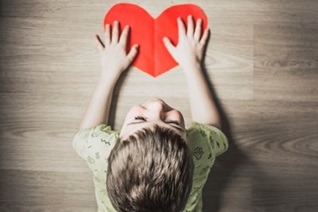 Depression - Photo by Anna Kolosyuk on Unsplash boy lay on stomach on floor with hands on a red paper heart