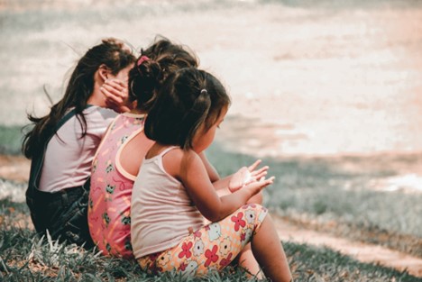 Three girls sitting on the curb of a parking lot.