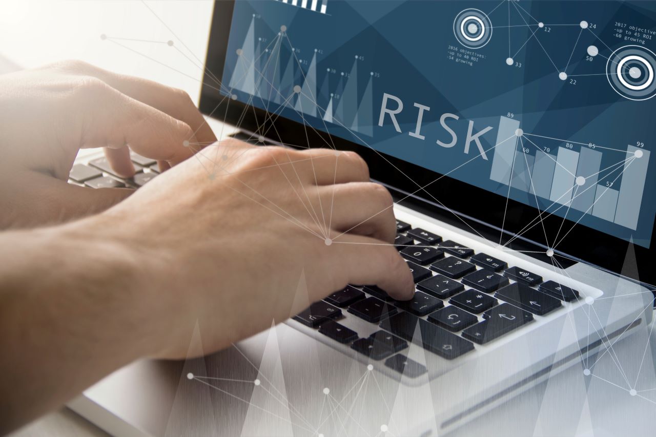 Image of hands on a keyboard while the screen shows data points and the word RISK.