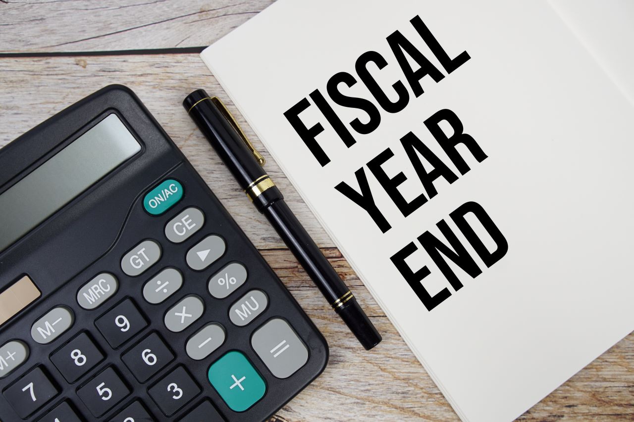 Image of a calculator beside a pen and paper. The paper reads fiscal year end.